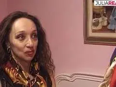 Ältere Frau mit dunklen Locken saugt hingebungsvoll an einem dicken Schwanz auf rosa Couch