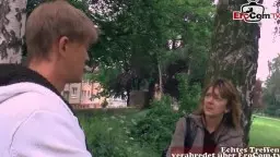 Blonde Cosplay-Schlampe in enger Jacke lehnt lasziv an Baum im Park und blickt den Mann in weißem Hoodie verführerisch an