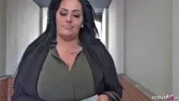 Vollbusige dunkelhaarige Milf mit hochgesteckten Haaren lehnt lustvoll stöhnend an einer Betonwand