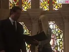 Blonde Frau im hellen Kleid wird von Mann im Anzug vor Kirchenfenster verfolgt