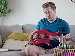 Attraktiver Mann mit Bart spielt im Wohnzimmer konzentriert eine rote Bassgitarre auf dem Sofa