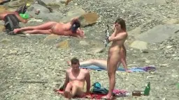 Zwei nackte Frauen liegen am steinigen Strand neben einem Mann