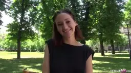 Junge Frau mit braunem Haar sitzt lächelnd auf sonniger Parkbank umgeben von grünen Bäumen
